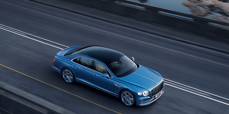 Bentley Panama New Bentley Flying Spur Azure sedan in Light windsor blue paint by Mulliner, with 22 inch Azure wheels seen from overhead driving dynamically on a country road