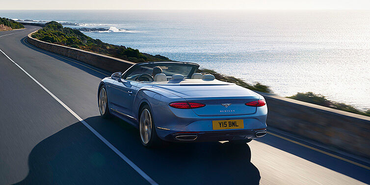 Bentley Panama New Bentley Continental GTC Azure convertible rear view in Light Windsor blue paint with 22 inch ten spoke wheels driving dynamically on an ocean road in the sunshine