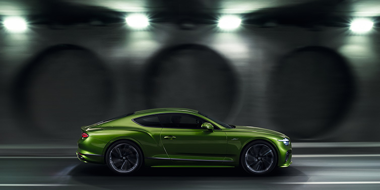 Bentley Panama Bentley Continental GT Speed coupe profile in Tourmaline Green driving dynamically past a concrete wall at night