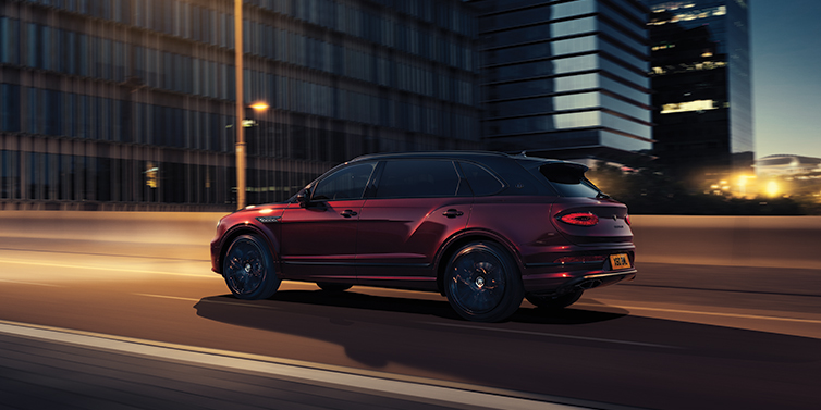Bentley Panama Bentley Bentayga Extended Wheelbase Mulliner SUV in Cricket Ball red paint driving dynamically in city at night